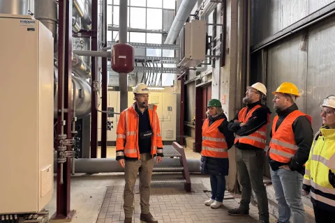 Ein Stadtwerkemitarbeiter mit typischer Arbeitsbekleidung steht im Heizkraftwerk und gibt Auskunft bei einer Führung.