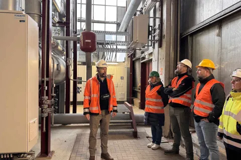 Ein Stadtwerkemitarbeiter mit typischer Arbeitsbekleidung steht im Heizkraftwerk und gibt Auskunft bei einer Führung.
