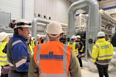 Ein Stadtwerkemitarbeiter mit typischer Arbeitsbekleidung steht vor Hochleistungswärmepumpen und gibt Auskunft zur Funktionsweise bei einer Führung.
