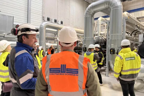 Ein Stadtwerkemitarbeiter mit typischer Arbeitsbekleidung steht vor Hochleistungswärmepumpen und gibt Auskunft zur Funktionsweise bei einer Führung.