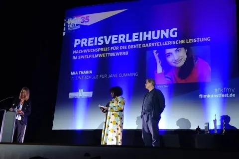 Aufnahme der Bühne beim Filmkunstfest MV mit Moderatorin. Der Screen zeigt die Gewinnerin des Nachwuchsdarstellerpreises.