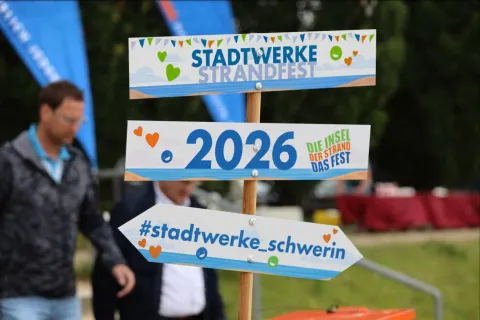 bunter Wegweiser mit drei Hinweisschildern: Stadtwerke-Strandfest , 2026, #stadtwerke_schwerin