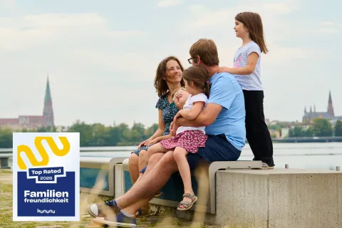 Eine fünfköpfige Familie sitzt am Hafen des Ziegelinnensees vor der Stadtsilouhette von Schwerin.