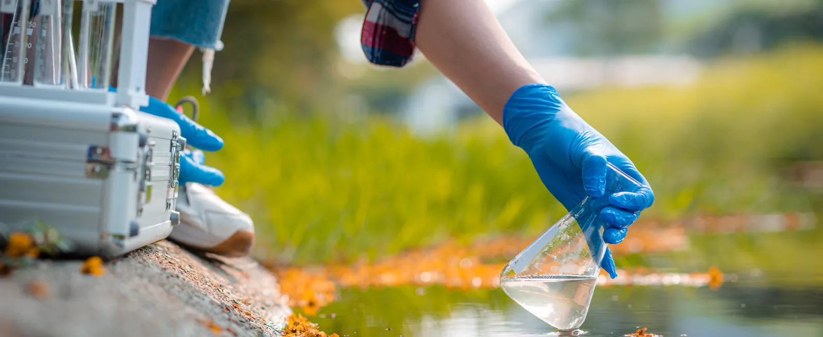 Hand eines Wissenschaftlers, der eine Wasserprobe aus einem See entnimmt