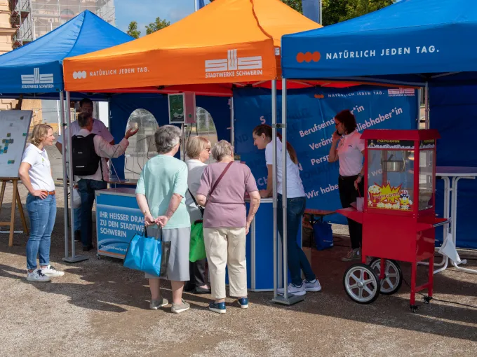 drei Pavillons der Stadtwerke stehen nebeneinander, in diesen sind Stehtische, Mitmachaktionen und Mitarbeitende, davor steht eine Gruppe von Passanten