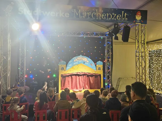 Blick auf eine Bühne mit Puppentheater. Davor sitzt Publikum.