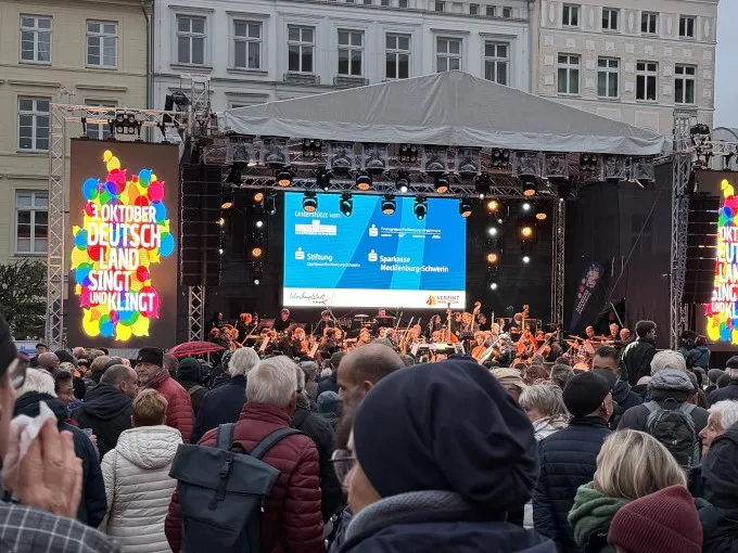 Vor einer großen Bühne auf einem Marktplatz stehen viele Menschen