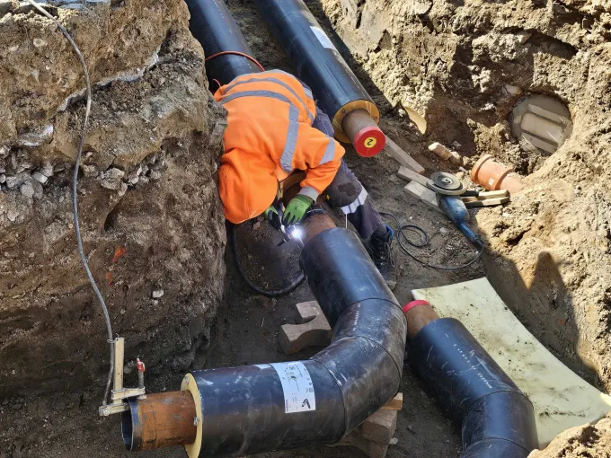 Ein Mann mit Arbeitsschutzbekleidung schweißt in einem Graben an einem großen schwarzen Rohr.