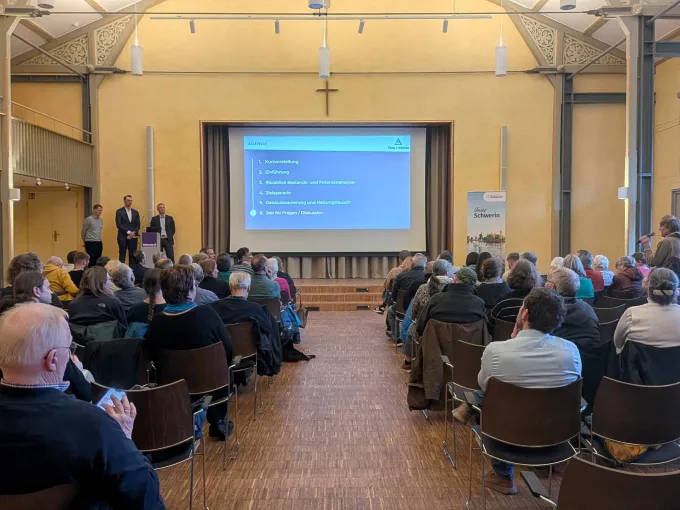 Menschen sitzen in einem Saal und schauen auf eine Präsentation