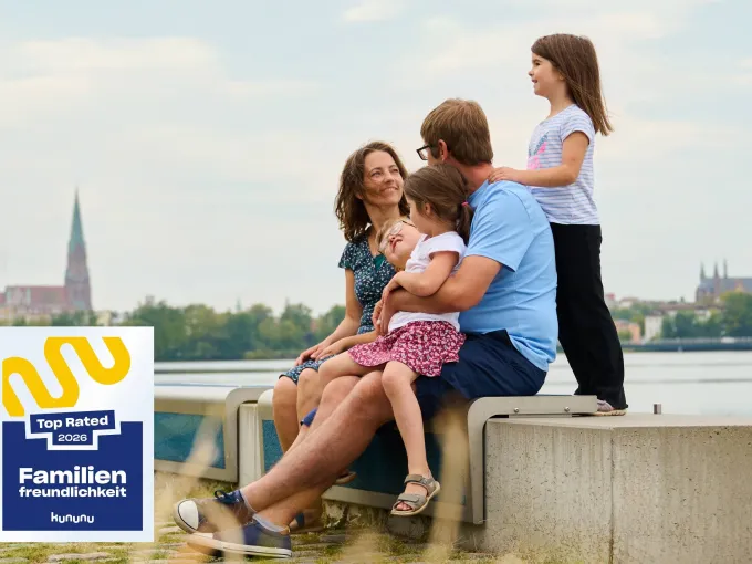 Eine fünfköpfige Familie sitzt am Hafen des Ziegelinnensees vor der Stadtsilouhette von Schwerin.
