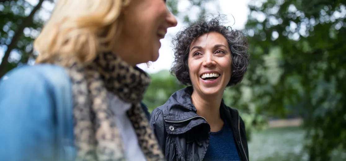 Zwei Freundinnen gehen im Wald spazieren und lächeln sich an.
