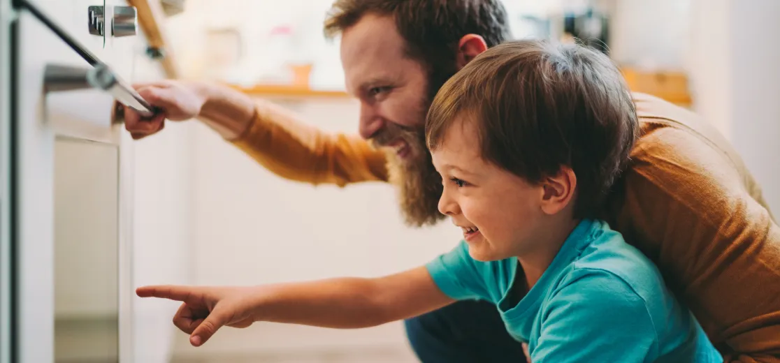 Vater und Sohn schauen begeistert in einen Backofen.