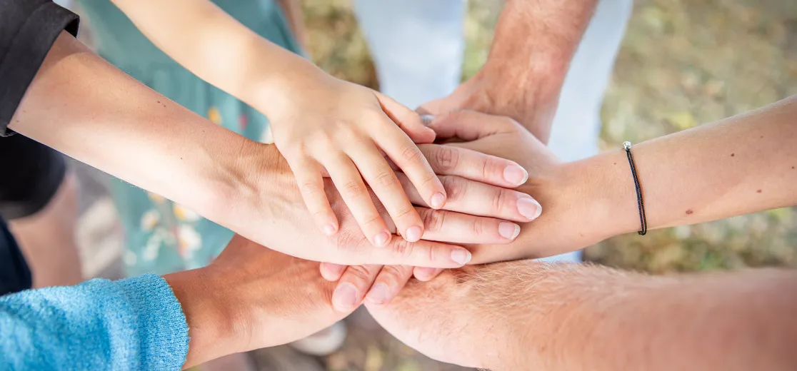 Sechs Hände von Männern, Frauen und Kindern übereinander gelegt.