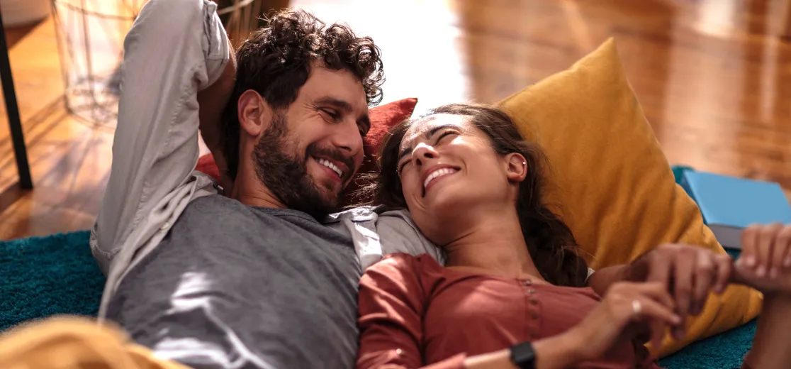Ein junges Paar liegt gemeinsam auf dem Sofa und lächelt sich an.