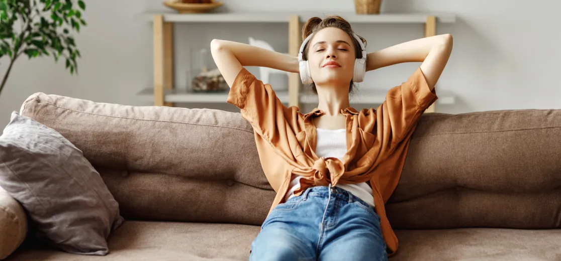 Eine junge Frau sitzt entspannt mit Kopfhörern auf dem Sofa.