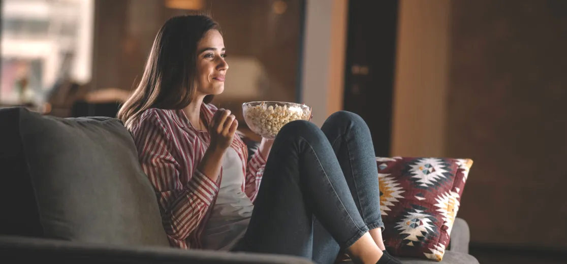 Eine Frau sitzt auf dem Sofa mit Popcorn in der Hand und schaut einen Film in der Nacht.
