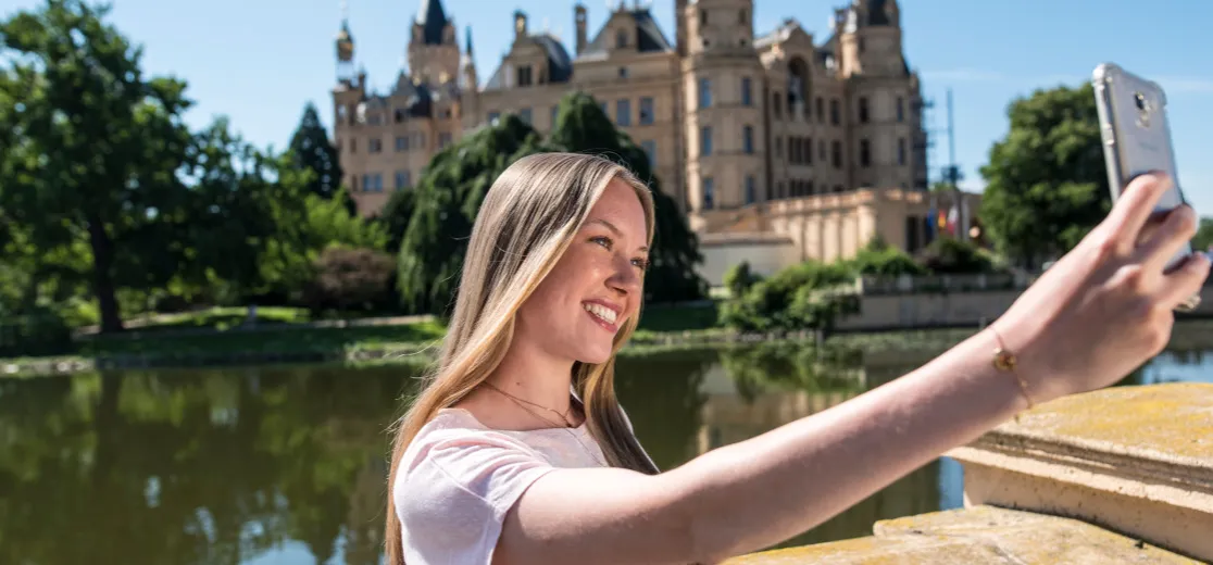 Eine Frau nimmt ein Selfie vor dem Schweriner Schloss von sich auf.