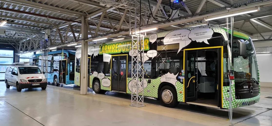 Ein bunt bedruckter Elektrobus in einer Halle des Nahverkehr Schwerins, dahinter steht ein blauer Bus.