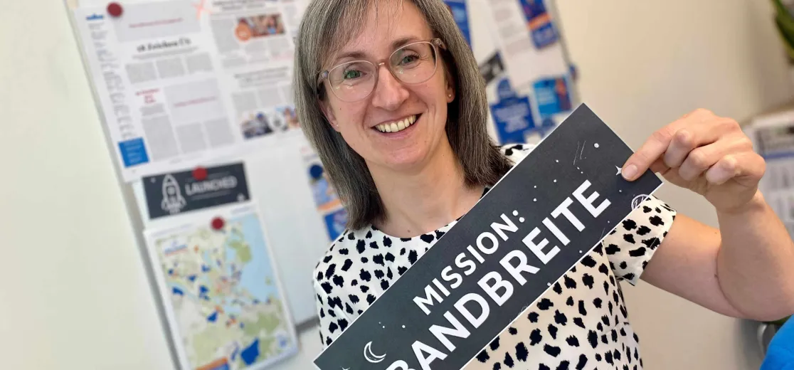 Frau im Büro mit Schild "Mission Bandbreite"