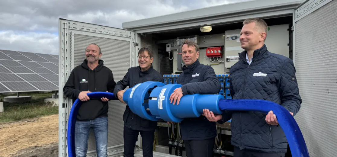 Vier Männer stehen vor einem Trafoschrank und halten einen großen Stromstecker
