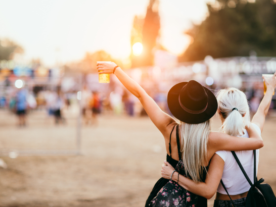 Zwei Frauen feiern am Strand. Beide halten ein Getränk in der Hand.