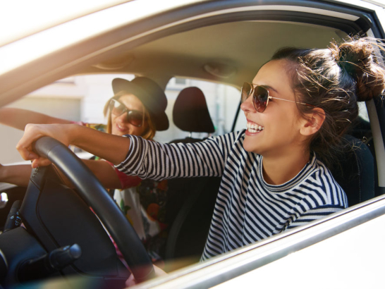 Zwei junge Frauen fahren im Auto und haben Spaß.