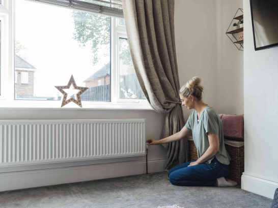 Eine Frau dreht am Heizungsthermostat, um Energie zu sparen.