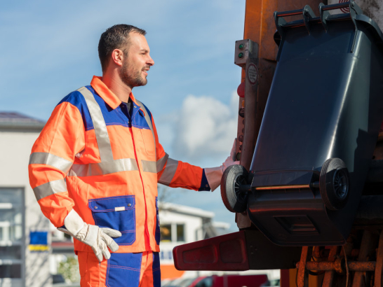 Mann leert Abfalltonne im LKW