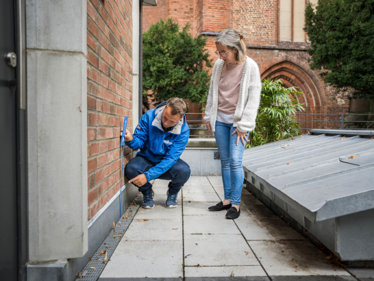 Ein Mitarbeiter der Stadtwerke Schwerin misst mit einem Zollstock an der Hauswand.