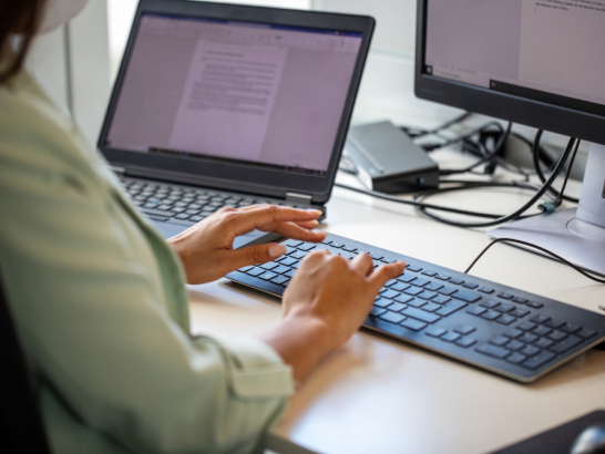 Nahaufnahme einer Frau, die am Arbeitsplatz auf der Computertastatur tippt.