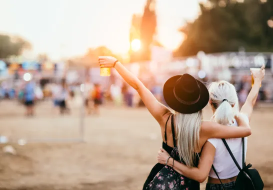 Zwei Frauen feiern am Strand. Beide halten ein Getränk in der Hand.