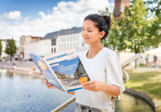 Eine junge Frau liest ein Stadtwerke-Magazin am Schweriner Pfaffenteich.