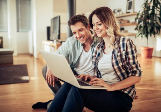 Ein Mann und eine Frau sitzen mit einem Laptop auf dem Sofa.