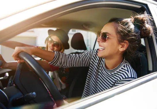 Zwei junge Frauen fahren im Auto und haben Spaß.