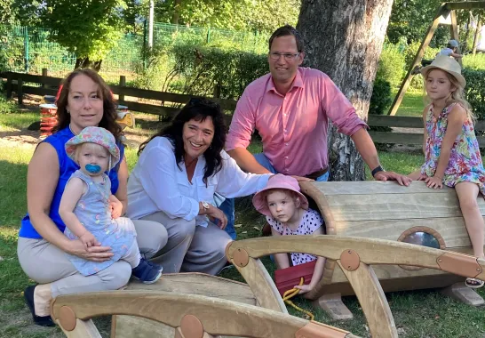 Zwei Frauen und ein Mann hocken bei Outdoor Bauelementen aus Holz mit drei spielenden Kindern