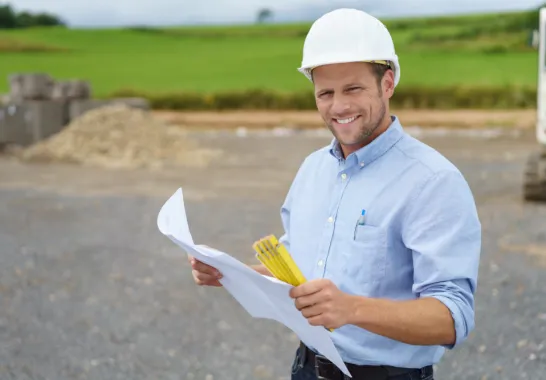 Ein Bauarbeiter mit einem Bauplan in der Hand lächelt in die Kamera.