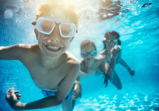 Kinder schwimmen im Pool und lächeln in die Kamera.