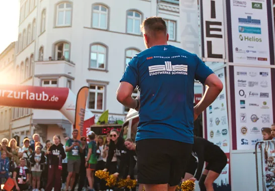 Zieleinlauf vom Schweriner Nachtlauf auf dem Markt mit tiefstehender Sonne, Stadtwerke Läufer von hinten 