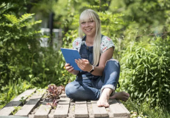 Eine Frau sitzt mit einem Tablet im Garten.