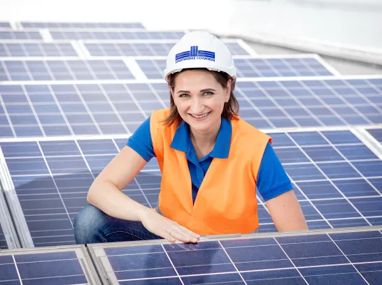 Eine junge Frau mit Warnweste und Helm kniet zwischen Solarmodulen.