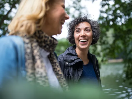 Zwei Freundinnen gehen im Wald spazieren und lächeln sich an.