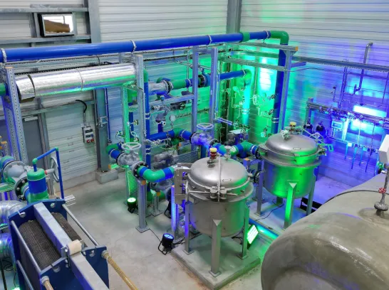 Innenaufnahme des SWS Geothermie-Heizwerks in Schwerin. Zu sehen sind mehrere Kessel, Rohre und Pumpen in beleuchteter Umgebung.