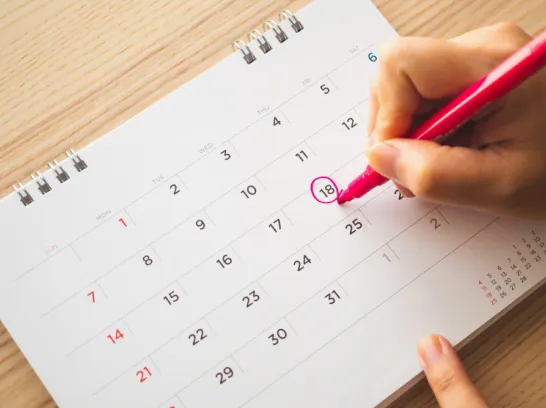 Eine Hand markiert einen Termin im Kalender.