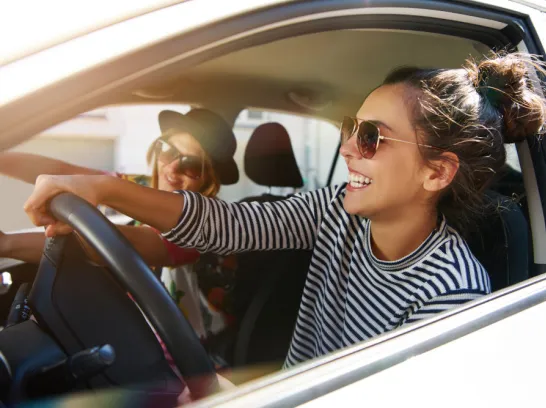 Zwei junge Frauen fahren im Auto und haben Spaß.