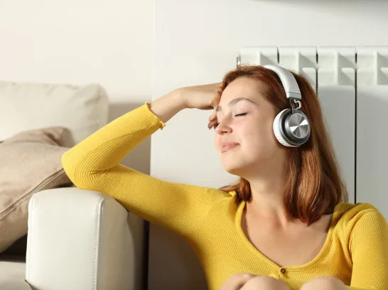 Eine Frau lehnt entspannt an der Heizung und hört Musik.