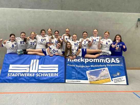 Mannschaftsfoto von Frauen in Meckpommgas-Trikots, im Vordergrund Banden mit Logo Stadtwerke Schwerin und MeckpommGas.