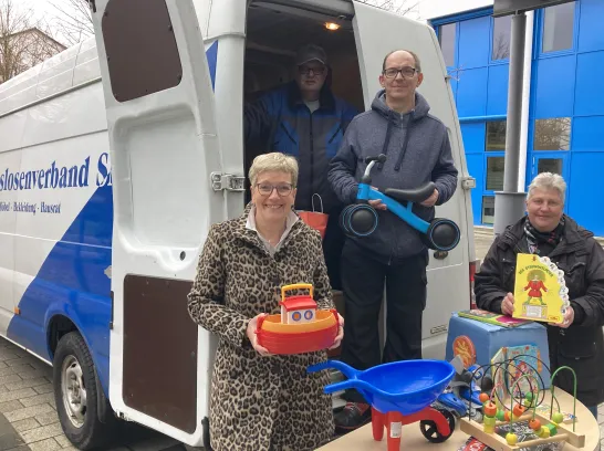 Vor einem Transporter vom Arbeitslosenverband Schwerin präsentieren Frauen und Männer gespendete Spielsachen.