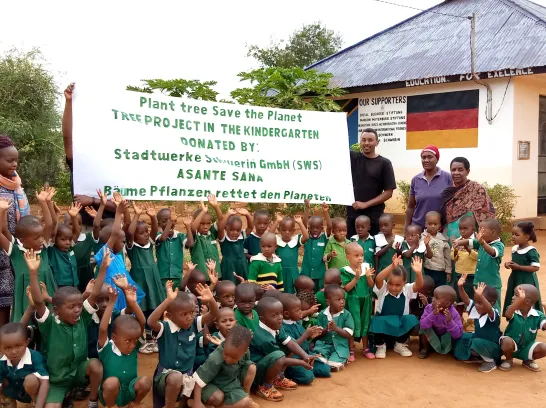 Eine Gruppe von afrikanischen Kindern in Schuluniform sitzt vor einem Banner mit Dankesgruß an die Stadtwerke Schwerin.