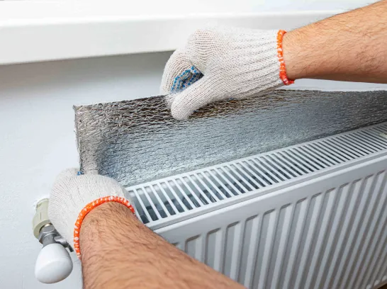 Ein Mann bringt eine Reflexionsfolie hinter seiner Heizung an.