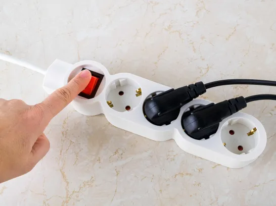 Eine Person bedient die Steckdosenleiste, um Strom zu sparen.